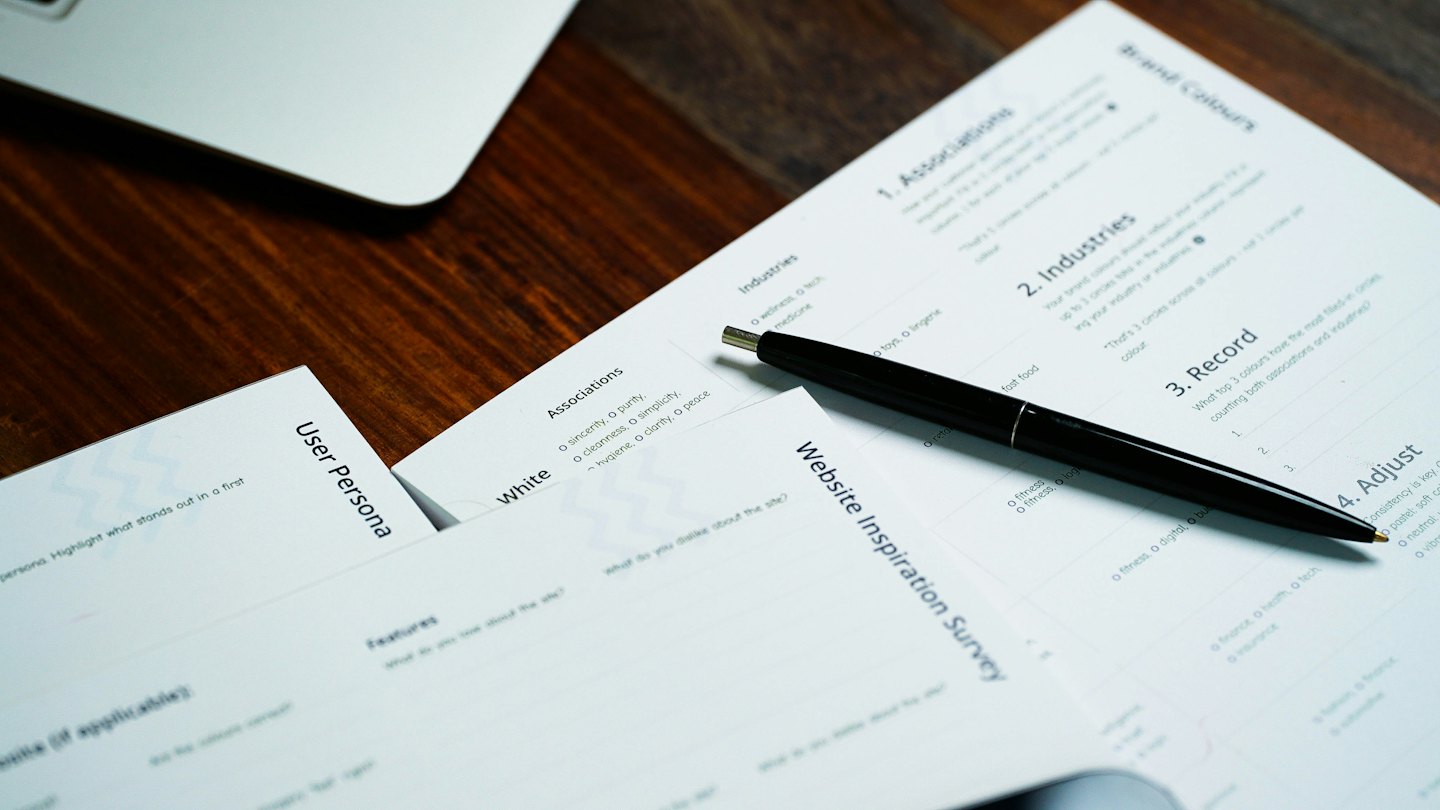 Pracovní stůl z masivního dřeva s dokumenty a notebookem.